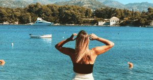 Woman gazing out at the calm Adriatic sea near Dubrovnik, phone nowhere in sight, boats gently anchored in the bay behind her.