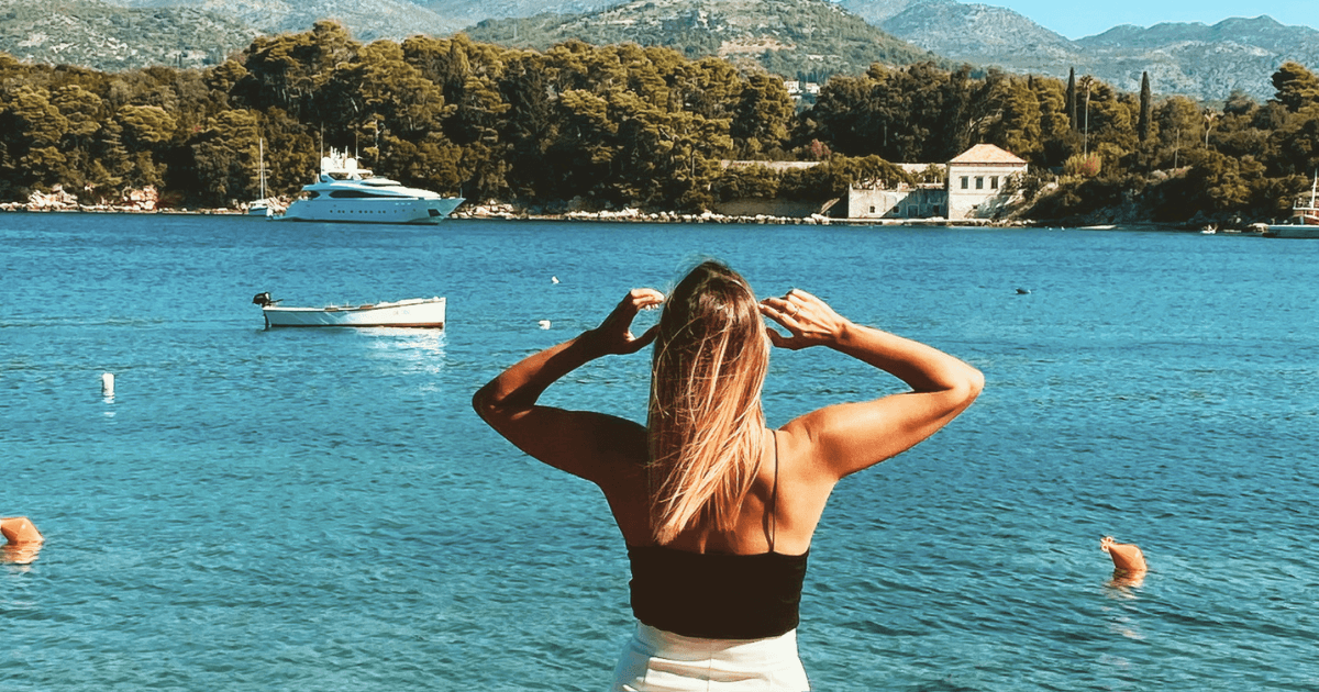 Woman gazing out at the calm Adriatic sea near Dubrovnik, phone nowhere in sight, boats gently anchored in the bay behind her.